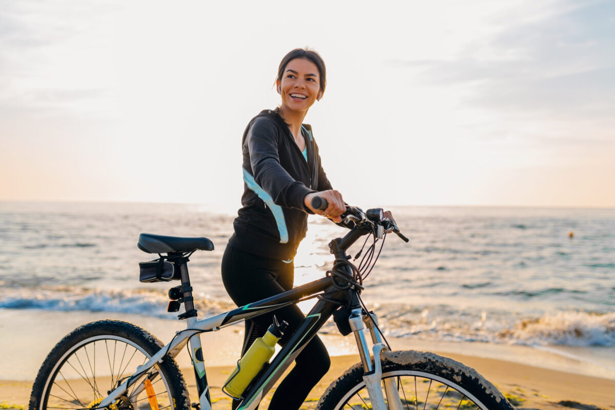 young attractive slim woman riding bicycle, sports on morning sunrise beach in sports fitness sport clothes, active healthy lifestyle, smiling happy having fun